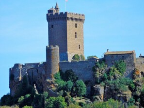 A historic stone castle with a prominent tower, surrounded by lush greenery and rocky terrain.