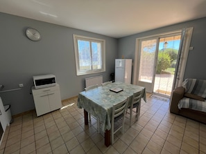 Un comedor con mesa, sillas, un reloj, un refrigerador y un sofá.