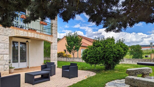 Un patio con mobiliario exterior, un muro de piedra y vista a un edificio con balcón.