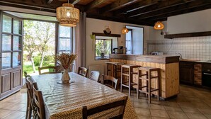 Une cuisine rustique avec un îlot central en bois, un coin repas avec une table et des chaises, et de grandes fenêtres laissant entrer la lumière naturelle.