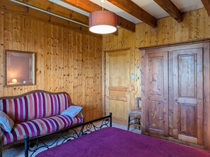 A wooden room with a bed, a striped sofa, a chair, and a wardrobe.
