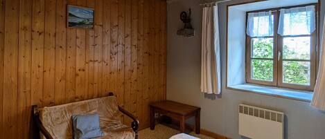 A room with wooden walls, a bed, a bench, a window with curtains, and a hanging light fixture.