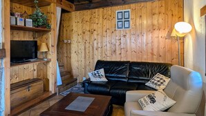 Une pièce aux murs lambrissés, avec un canapé en cuir noir, un téléviseur et une lampe.