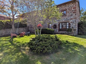 A stone building with a red-tiled roof, a well-maintained lawn, and outdoor seating.