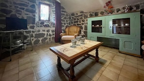 A room with a stone wall, a wooden table, a green cabinet, and a chair. - Cozy Cottage Near Mézenc Plateau - Calm Hamlet, Golf Nearby, Baby Gear Included (Lantriac)