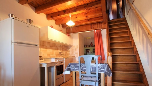 A compact kitchen with a refrigerator, stove, oven, and a dining table with chairs. - Cozy Cottage Near Mézenc Plateau - Calm Hamlet, Golf Nearby, Baby Gear Included (Lantriac)