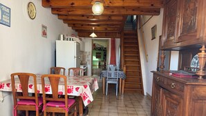 Un coin repas avec une table et des chaises en bois, une cuisine à l’arrière-plan et un escalier menant à l’étage.