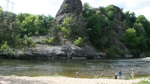 Paisagem natural com uma grande formação rochosa, um rio e uma área de praia arenosa.