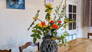 A dining table with a vase of flowers, wooden chairs, and artwork on the walls.