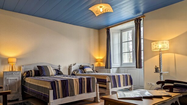 A hotel room with two beds, a desk, a chair, a lamp, and a window with curtains.