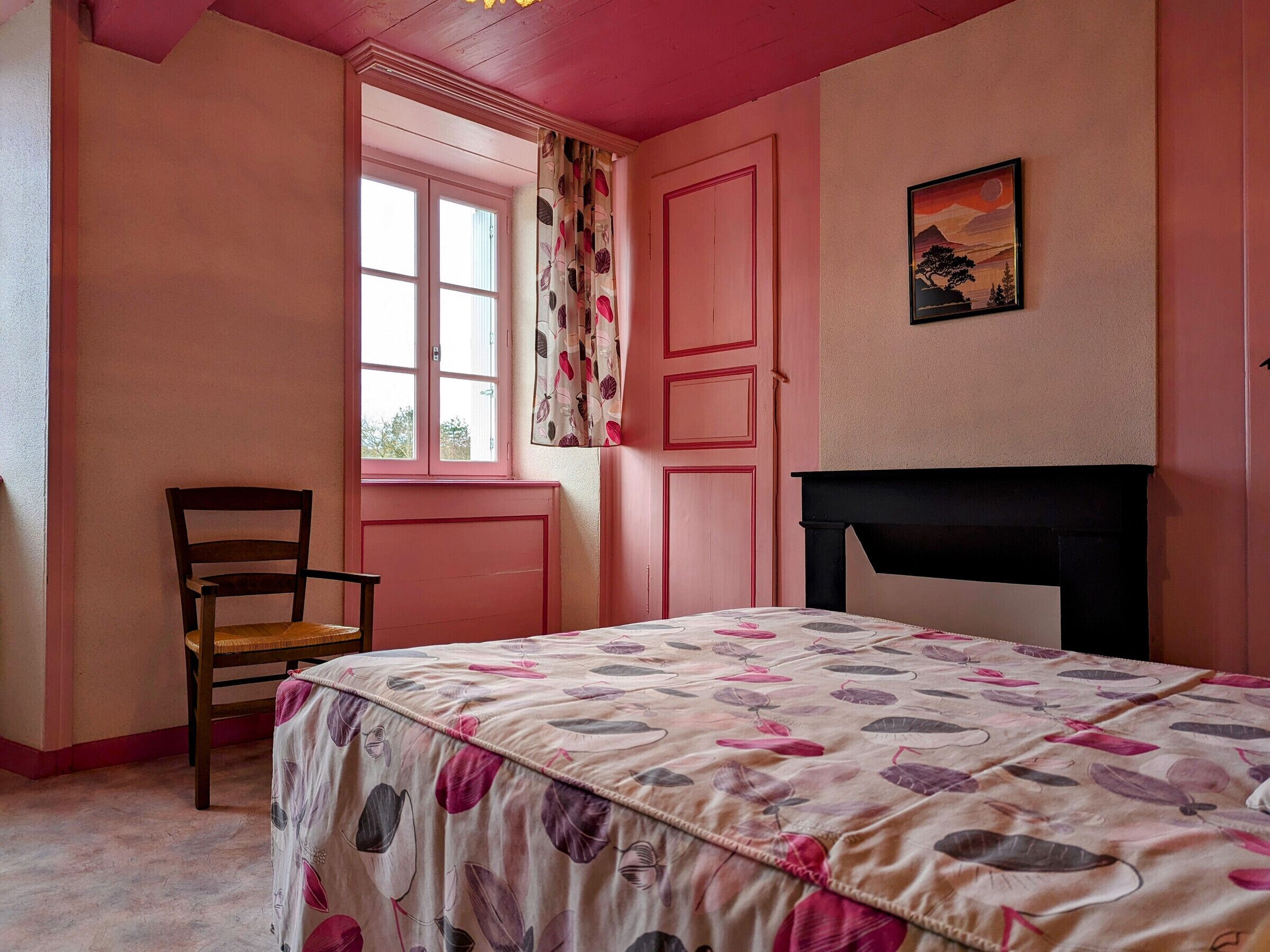 A bedroom with a bed, a chair, a window with curtains, and a painting on the wall.