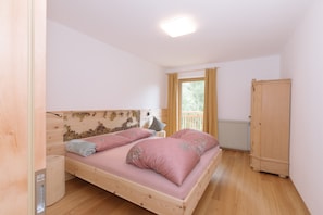 Un dormitorio con cama de madera, mesita de noche, armario y ventana con cortinas.