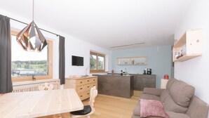A modern kitchen with wooden cabinets, a dining table, and chairs. There is a sofa with a cushion and a television on the wall. - Holiday Home “Berg Wieserhof” with Mountain View, Balcony and Shared Garden (Aldein)