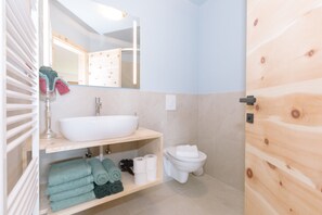 Une salle de bain avec un lavabo blanc, un miroir, des toilettes et une porte en bois.