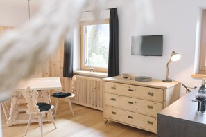 A room with a wooden table and chairs, a dresser, a radiator, a TV on the wall, and a window with curtains.