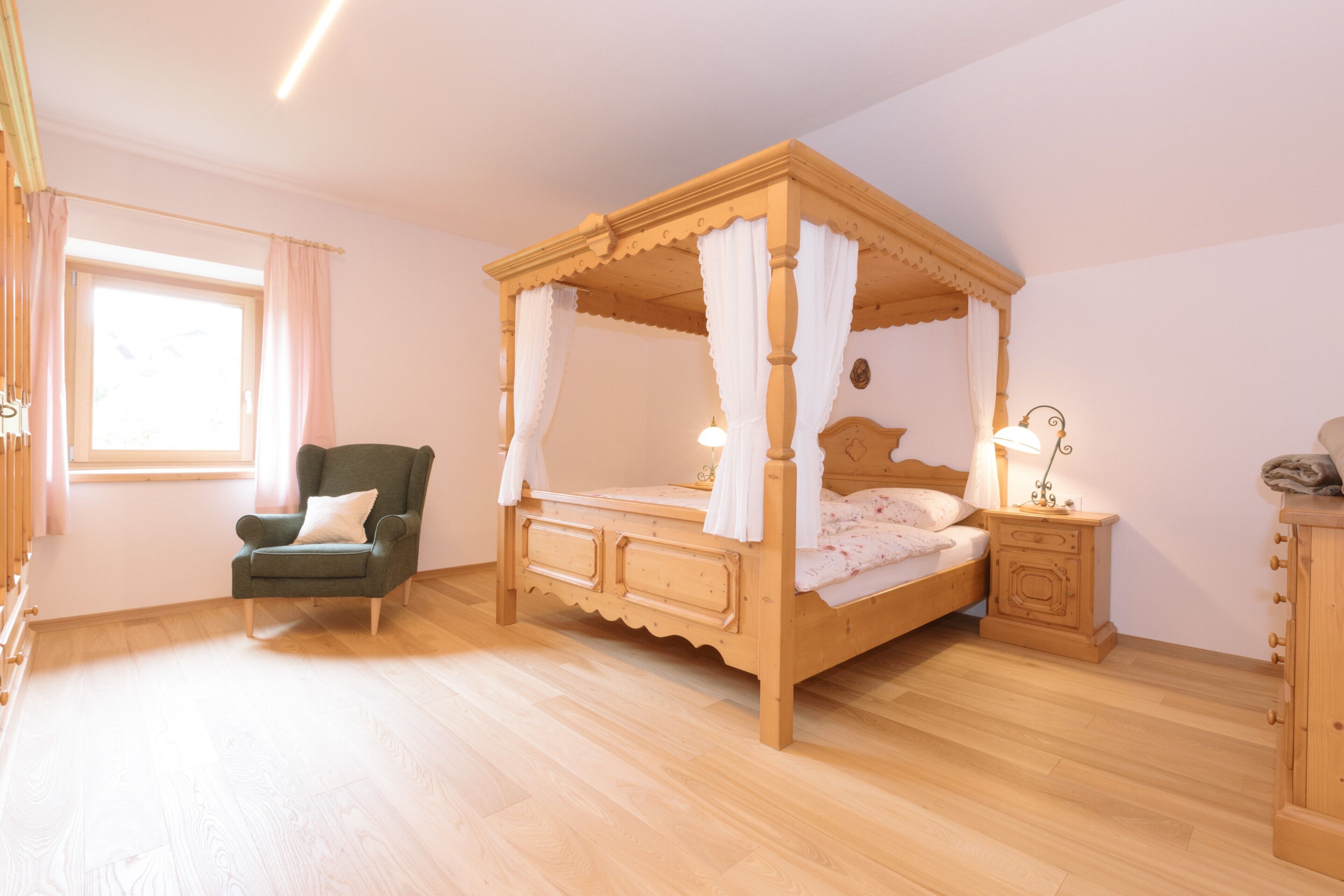 A four-poster bed with a canopy, a nightstand with a lamp, a chair, and a dresser.