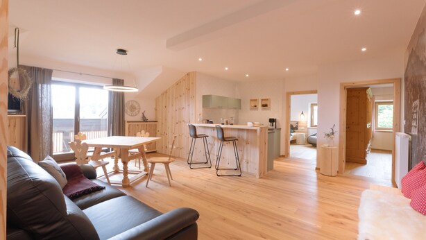 A modern living room with a sofa, a dining table, and a kitchen area with wooden cabinets and a bar. - Holiday Home “Wies Wieserhof” with Mountain View, Balcony and Shared Garden (Aldein)