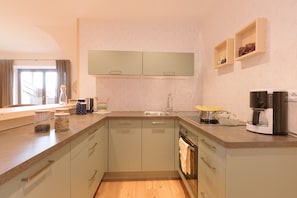 A modern kitchen with a built-in oven, a coffee maker, and a window with curtains.