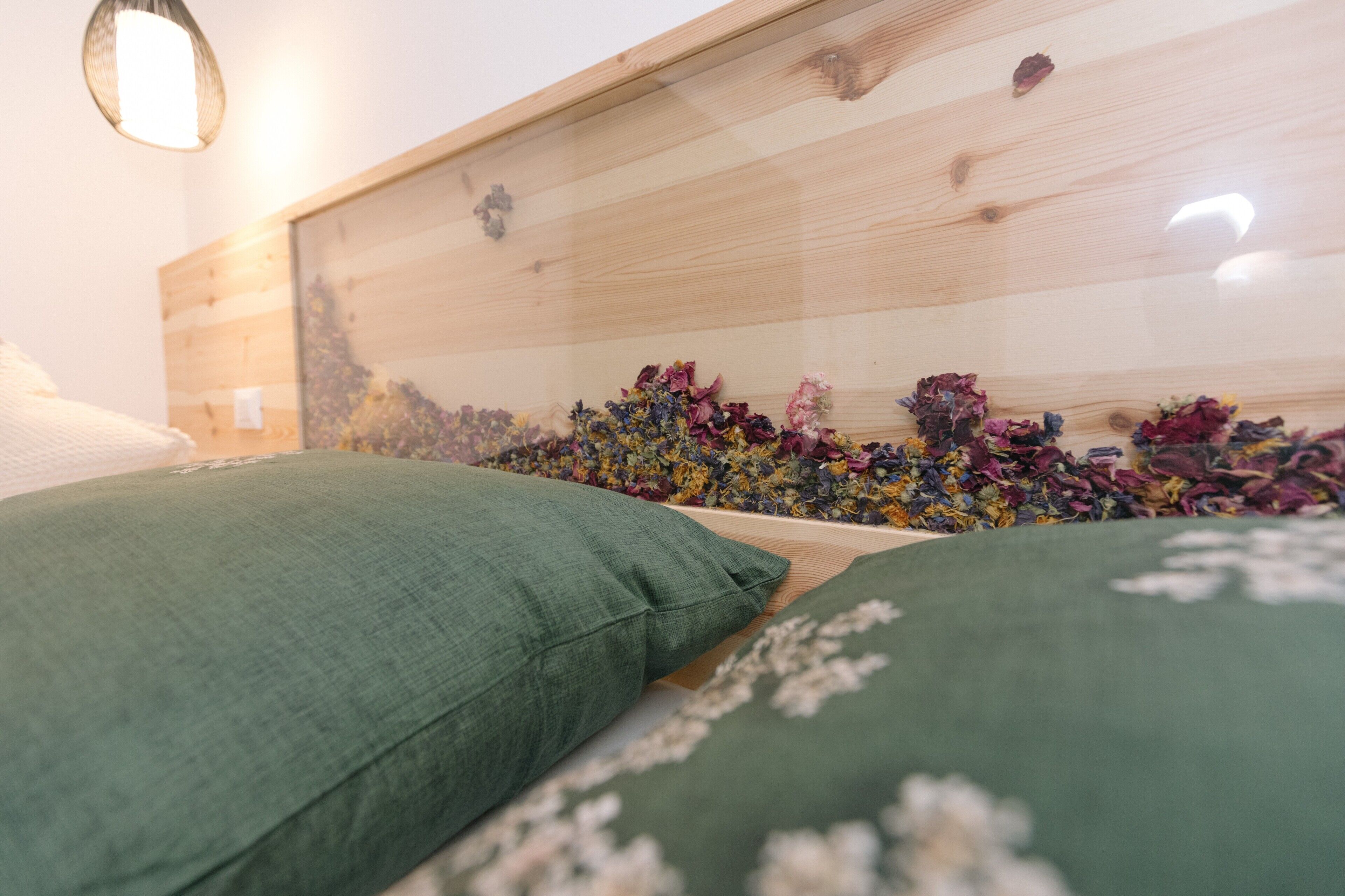 Una cama con almohadas verdes, un cabecero de madera y una pared decorada con flores secas.