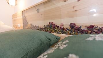 Una cama con almohadas verdes, un cabecero de madera y una pared decorada con flores secas.