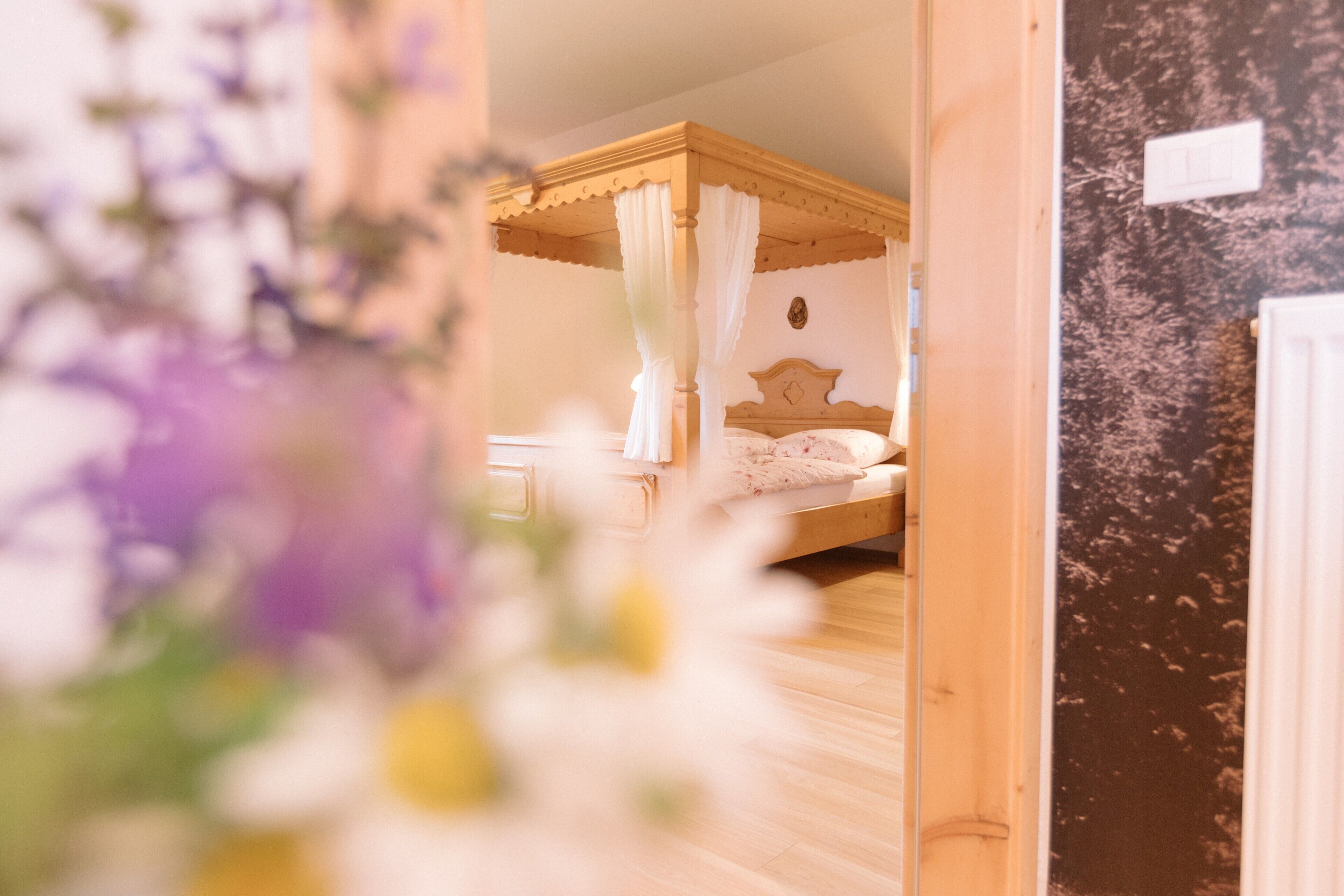 Une chambre à coucher avec un lit à baldaquin, un plancher en bois et un interrupteur fixé au mur.