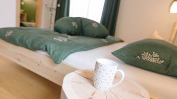 Una cama con ropa de cama verde y una taza blanca sobre un taburete de madera.