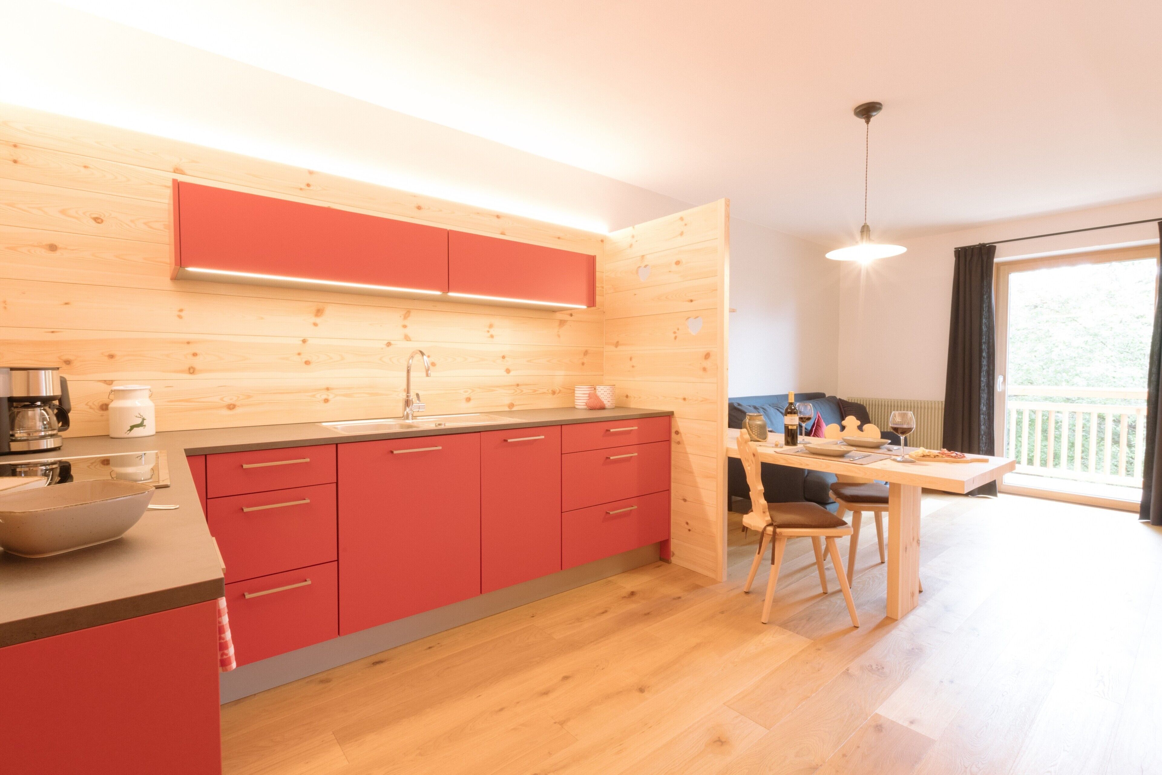 Une cuisine moderne avec des meubles de rangement rouges, un plan de travail en bois et un coin repas comprenant une table et des chaises.