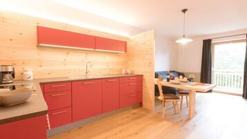 Une cuisine moderne avec des meubles de rangement rouges, un plan de travail en bois et un coin repas comprenant une table et des chaises.