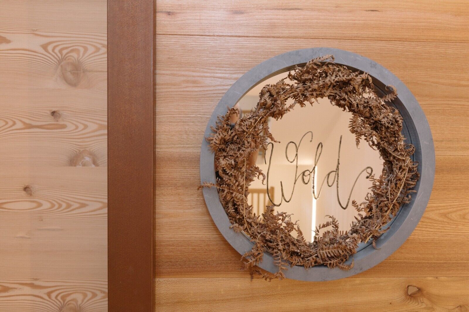 Una placa de madera circular con una palabra escrita a mano, rodeada de follaje seco.