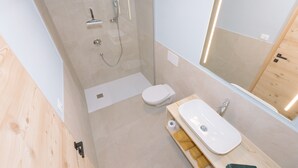 Et moderne badeværelse med en bruseniche i glas, et hvidt toilet, en vask med spejl og trægulv.