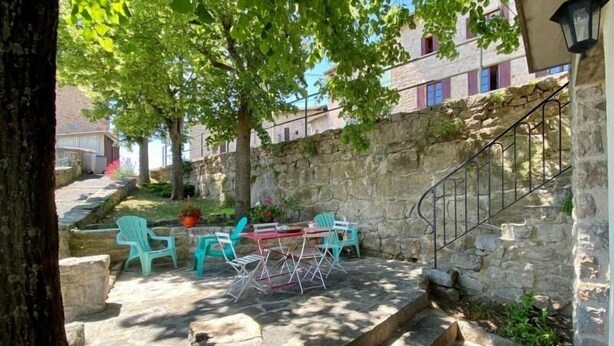 A stone staircase leading up to a building with a stone wall and a metal railing. There are outdoor tables and chairs under a tree. - Charming Cottage Near Puy-en-Velay with Private Terrace and Modern Amenities (Blavozy)