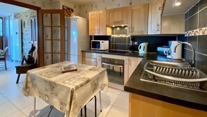 A modern kitchen with wooden cabinets, a stainless steel sink, and a dining table set with a tablecloth. - Charming Cottage Near Puy-en-Velay with Private Terrace and Modern Amenities (Blavozy)