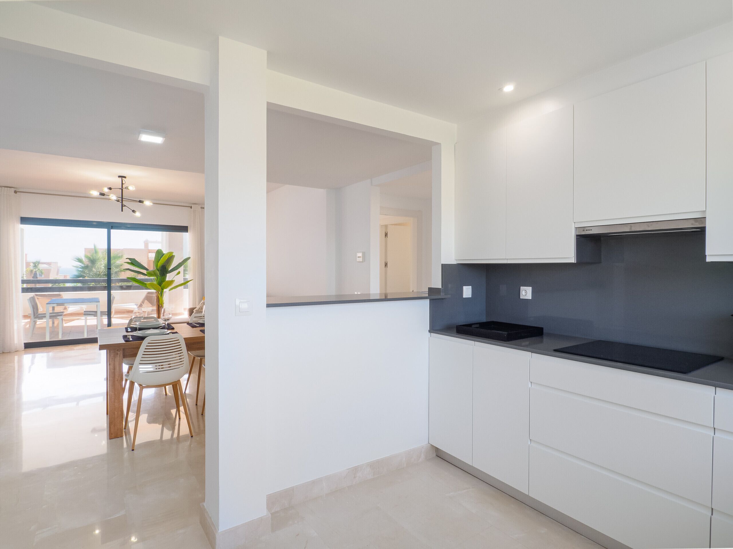 A modern kitchen with white cabinets, a black countertop, and a Bosch range hood.