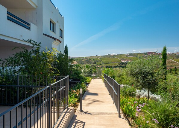 A pathway leading to a white building with multiple windows, surrounded by lush greenery and a clear blue sky. - Lotus Golf & Beach 2306 (Casares)
