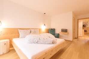 Un lit en bois avec une tête de lit, une lampe de chevet, une chaise de couleur turquoise et une étagère avec des serviettes.