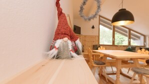 Un coin repas avec une table et des chaises en bois, une guirlande suspendue et une décoration représentant un gnome accrochée au mur.