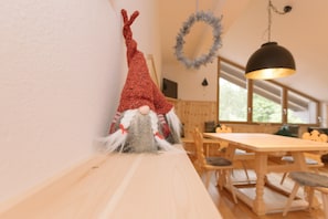 Un coin repas avec une table et des chaises en bois, une guirlande suspendue et une décoration représentant un gnome accrochée au mur.