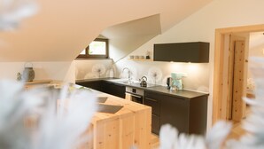 Une cuisine moderne dotée d’un îlot central en bois, d’appareils électroménagers intégrés et d’une fenêtre laissant entrer la lumière naturelle.