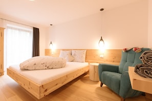 Un lit en bois avec une tête de lit, un fauteuil turquoise et une petite table de chevet.