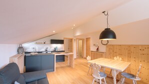 Une cuisine moderne dotée d’un îlot central, un coin repas avec une table et des chaises en bois, et un espace de vie chaleureux avec un canapé.