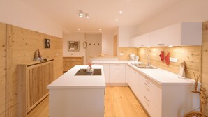 A modern kitchen with white cabinetry, a central island, and wooden accents on the walls. - Beautiful and Cozy Holiday Home “Ferienwohnung SHUPF Wieserhof” with Mountain View, Balcony, Shared Garden & WiFi; Parking Available (Aldein)