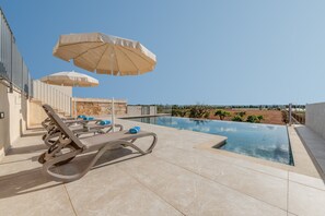 Une piscine sur le toit, agrémentée de chaises longues et de parasols, avec un ciel dégagé et une vue imprenable sur le paysage.
