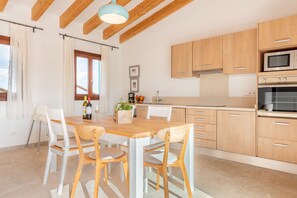 Eine moderne Küche mit Holzschränken, einem Esstisch mit Stühlen und einem Fenster mit Vorhängen.