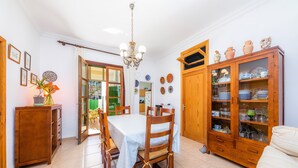 Un coin repas avec une table dressée pour quatre personnes, des chaises en bois, un lustre et un buffet dont les portes sont en verre et qui contient de la vaisselle.