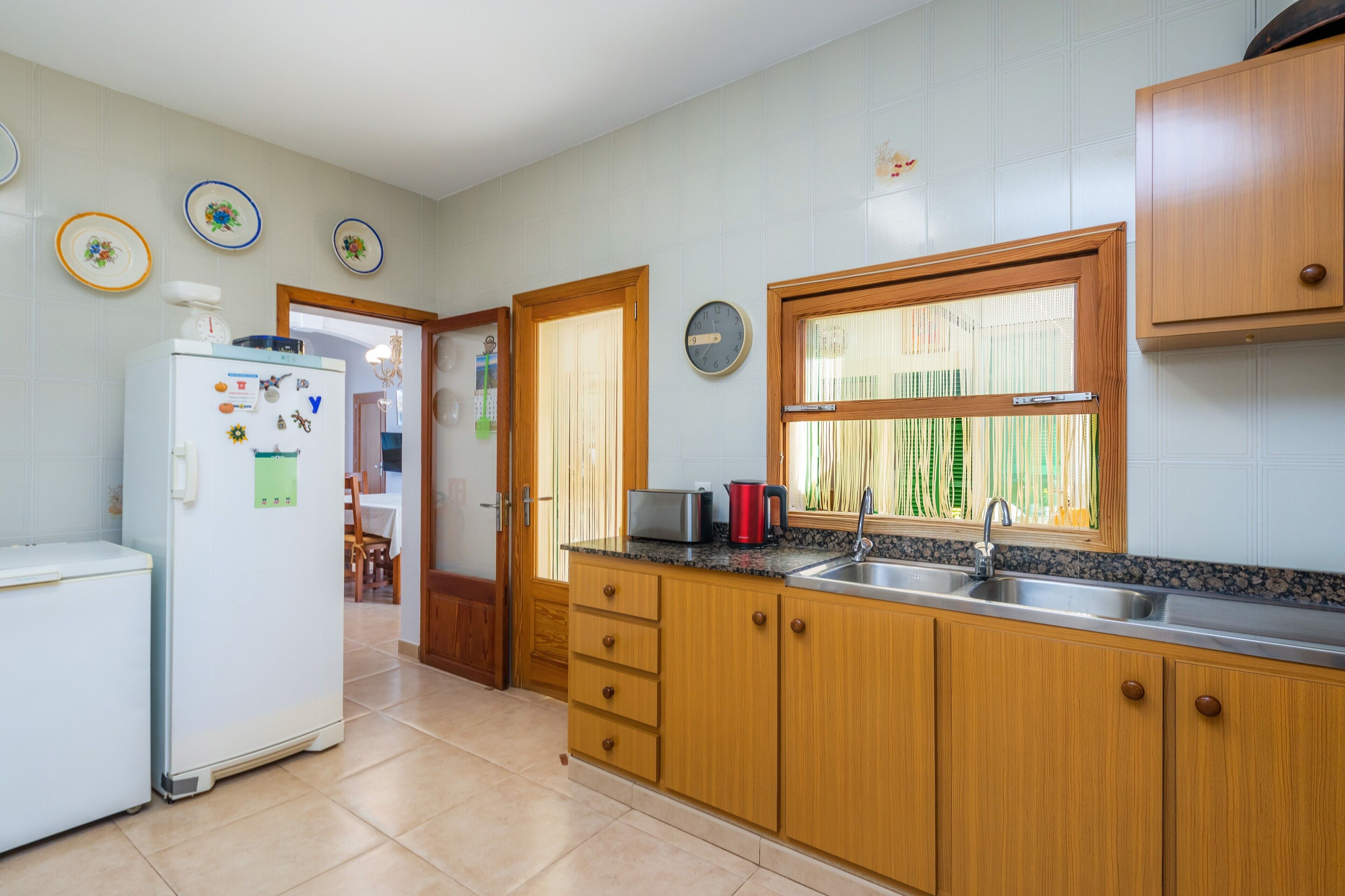 A kitchen with wooden cabinets, a refrigerator, a sink, and a window with blinds.