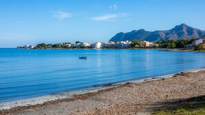 Une ville côtière avec des bâtiments qui bordent la plage, une mer d’un bleu limpide et une montagne en arrière-plan.
