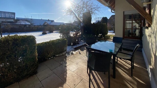 Un patio con mesa y sillas, vista a un paisaje nevado y un edificio con puerta de garaje.