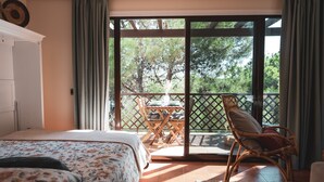 Een slaapkamer met een bed, een stoel, een tafel en een balkon met uitzicht op bomen.