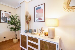 Une pièce bien éclairée, avec une console blanche, des objets décoratifs, une lampe et un tableau abstrait encadré accroché au mur.