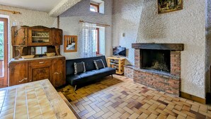 Una habitación rústica con pared de piedra, chimenea, un armario de madera, un sofá negro y un televisor.